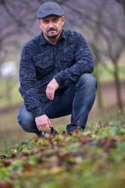 Kot pantolonlu ve kepli çiftçi kış başında meyve bahçesinde poz veriyor.