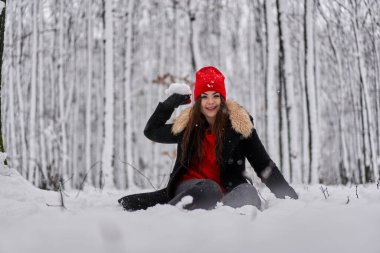 Kışın karlı bir ormanda kırmızı şapkalı beyaz bir kadının portresi.