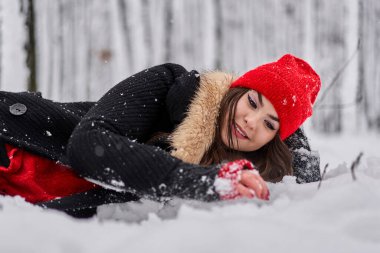 Kışın karlı bir ormanda kırmızı şapkalı beyaz bir kadının portresi.