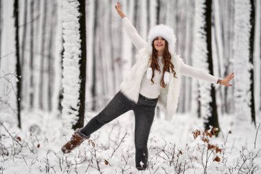 Genç beyaz kadın ormanda karda oynarken eğleniyor.