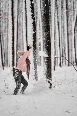 Genç beyaz kadın ormanda karda oynarken eğleniyor.