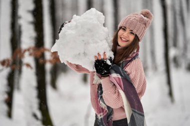 Genç beyaz kadın ormanda karda oynarken eğleniyor.