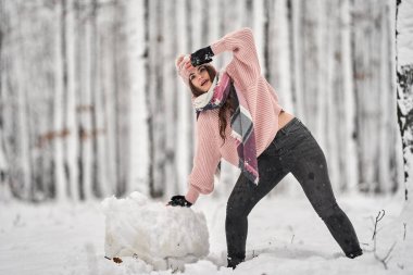 Genç beyaz kadın ormanda karda oynarken eğleniyor.