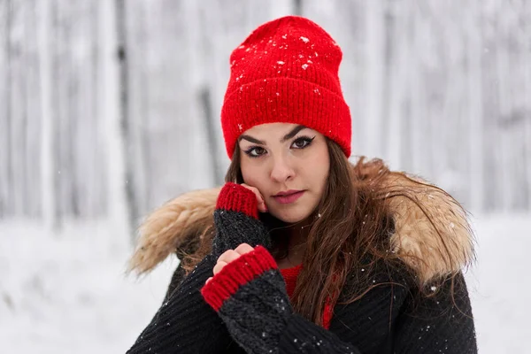 冬の雪深い森の中に赤いキャップを持つ若い白人女性の肖像画 — ストック写真