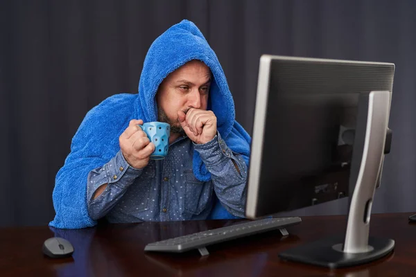 与Covid 19一起工作的商人在他的电脑上工作时 被厚厚的毛巾覆盖着 一边喝着热茶 — 图库照片