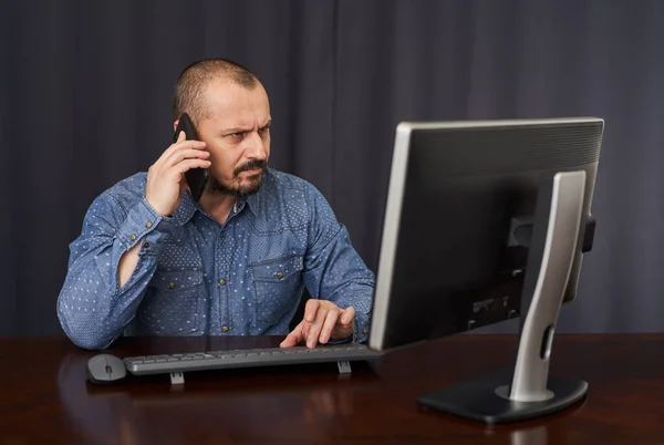 ビジネスマンは携帯電話で話をし 机の上で自分のコンピュータで作業する ストック写真