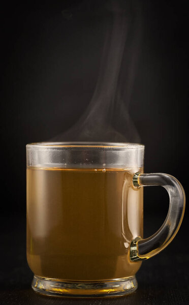 Steaming hot herbal chamomile tea in a glass mug on black background