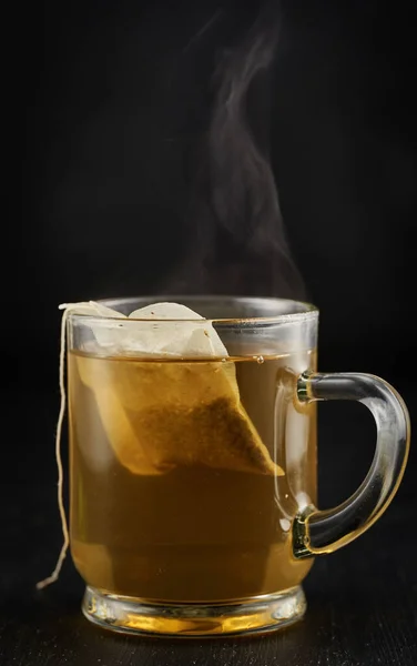 Steaming hot herbal chamomile tea in a glass mug on black background