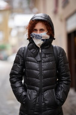Kışlık ceketli ve yüz maskeli bir kadın, Covid-19 salgını sırasında şehir portresi.