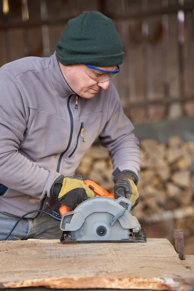 Carpenter using a hand circular saw with laser to cut a walnut board