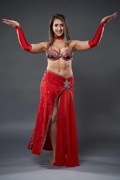 Arab woman belly dancer in red sparkling costume on gray background