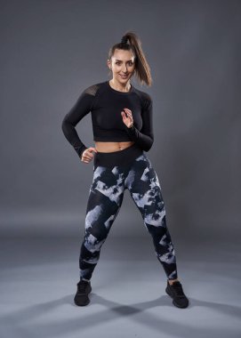 Kendine güvenen, kilolu, spor kıyafetli, gri arka planda egzersiz yapan genç bir kadın.