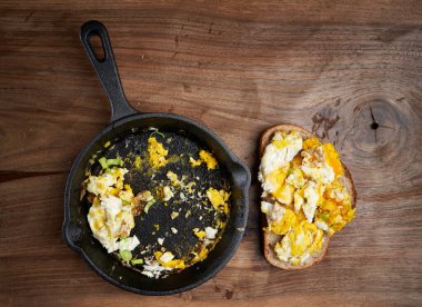 Bir dilim ekmeğin üzerinde çırpılmış yumurta, dökme demir bir tavanın yanında.