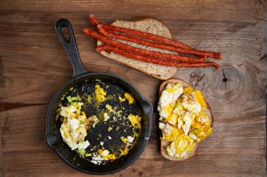 Dökme demir bir tavaya çırpılmış yumurta ve ahşap bir tahtaya sosis yapıştır, kahvaltı.