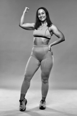 Ayrıca kendine güvenen genç bir kadın gri arka plan üzerinde spor yapıyor.