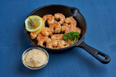 Lezzetli kırmızı kral karidesleri, dökme demir tavada mavi arka planda hazır.