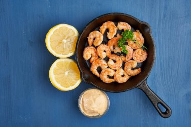 Lezzetli kırmızı kral karidesleri, dökme demir tavada mavi arka planda hazır.