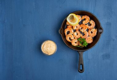 Lezzetli kırmızı kral karidesleri, dökme demir tavada mavi arka planda hazır.