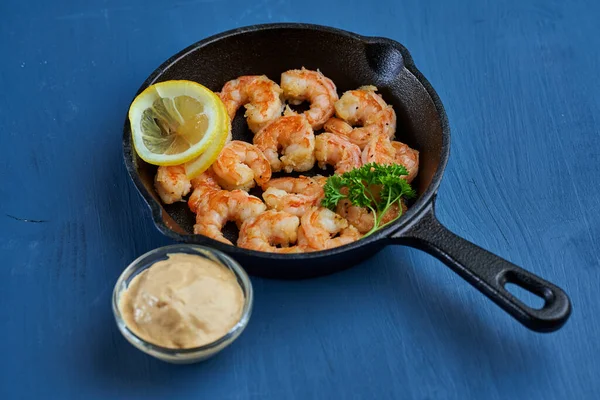 Lezzetli kırmızı kral karidesleri, dökme demir tavada mavi arka planda hazır.