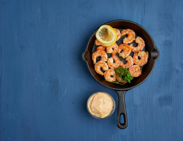 Lezzetli kırmızı kral karidesleri, dökme demir tavada mavi arka planda hazır.