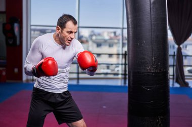 Kickboks dövüşçüsü spor salonunda kum torbasına vuruyor, yarışma için antrenman yapıyor.