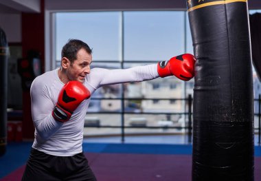 Kickboks dövüşçüsü spor salonunda kum torbasına vuruyor, yarışma için antrenman yapıyor.