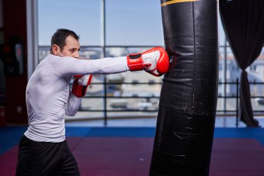 Kickboks dövüşçüsü spor salonunda kum torbasına vuruyor, yarışma için antrenman yapıyor.