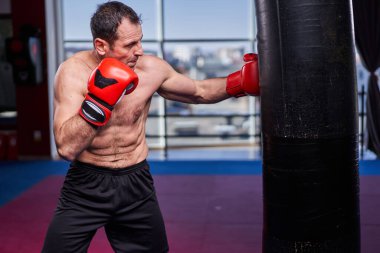 Kickboks dövüşçüsü spor salonunda kum torbasına vuruyor, yarışma için antrenman yapıyor.