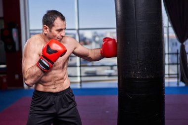 Kickboks dövüşçüsü spor salonunda kum torbasına vuruyor, yarışma için antrenman yapıyor.