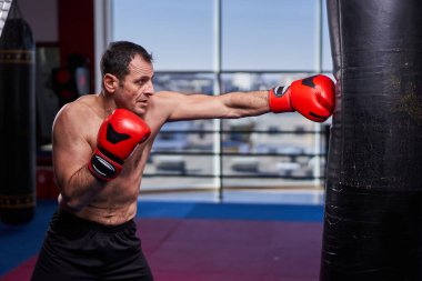 Kickboks dövüşçüsü spor salonunda kum torbasına vuruyor, yarışma için antrenman yapıyor.