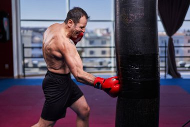 Kickboks dövüşçüsü spor salonunda kum torbasına vuruyor, yarışma için antrenman yapıyor.