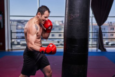 Kickboks dövüşçüsü spor salonunda kum torbasına vuruyor, yarışma için antrenman yapıyor.