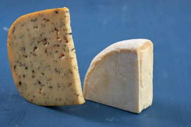 Mavi ahşap bir tahtanın üzerinde yıllanmış otlu çedar peyniri ve Camembert peyniri.