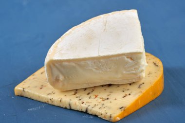 Mavi ahşap bir tahtanın üzerinde yıllanmış otlu çedar peyniri ve Camembert peyniri.