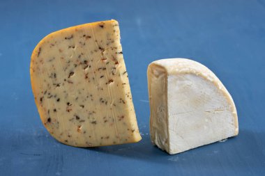 Mavi ahşap bir tahtanın üzerinde yıllanmış otlu çedar peyniri ve Camembert peyniri.