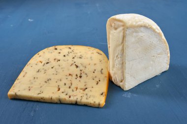 Mavi ahşap bir tahtanın üzerinde yıllanmış otlu çedar peyniri ve Camembert peyniri.