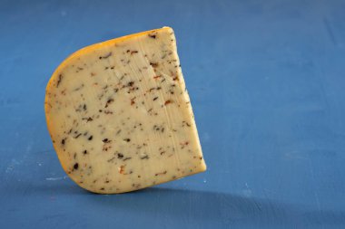 Mavi ahşap bir tahtanın üzerinde bitkiler ve baharatlarla yaşlanmış bir çedar peyniri.