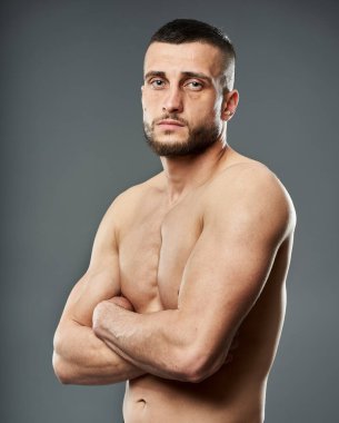 Gri arka planda yalnız poz veren genç üstsüz sporcu.