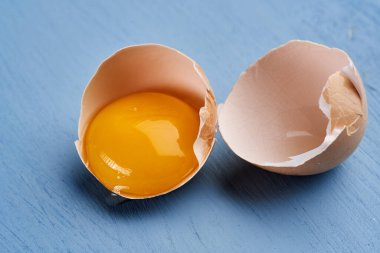 Mavi arka planda çiğ yumurta ve kırık kabuk.