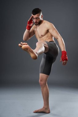 MMA dövüşçüsü bacak tekmesi atıyor, stüdyo çekimi gri arka planda izole edilmiş.