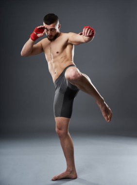 MMA dövüşçüsü bacak tekmesi atıyor, stüdyo çekimi gri arka planda izole edilmiş.