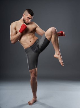 MMA dövüşçüsü diz vuruşu yapıyor, stüdyo çekimi gri arka planda izole edilmiş.