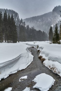 Kar fırtınasında dağlık bir nehir manzarası