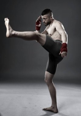 MMA dövüşçüsü bacak tekmesi atıyor, stüdyo çekimi gri arka planda izole edilmiş.