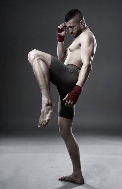 MMA dövüşçüsü diz vuruşu yapıyor, stüdyo çekimi gri arka planda izole edilmiş.