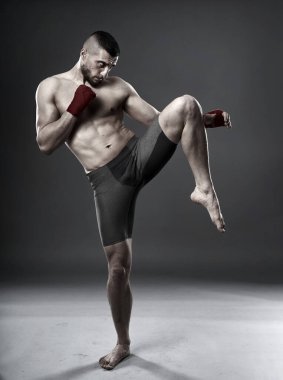 MMA dövüşçüsü diz vuruşu yapıyor, stüdyo çekimi gri arka planda izole edilmiş.
