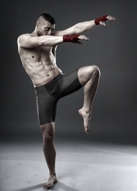 MMA dövüşçüsü diz vuruşu yapıyor, stüdyo çekimi gri arka planda izole edilmiş.