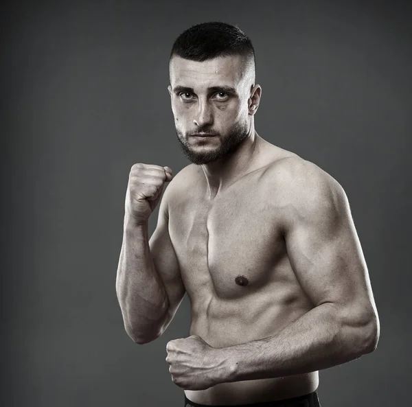 Young shirtless athletic fighter posing isolated on gray background