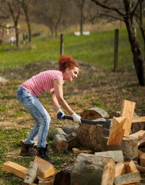 Kadın çiftçi arka bahçede yakacak odun bulmak için kayın kütüklerini kırıyor.