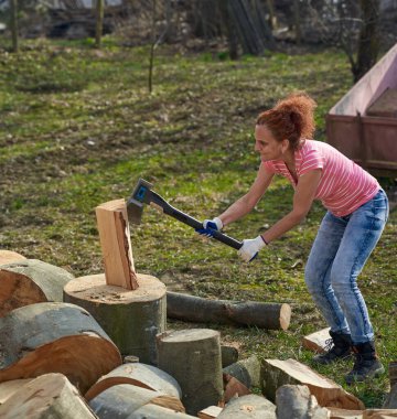 Kadın çiftçi arka bahçede yakacak odun bulmak için kayın kütüklerini kırıyor.